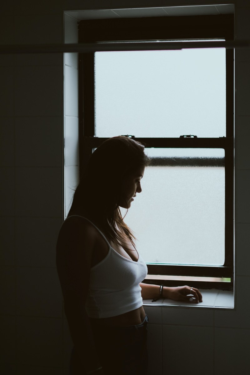 silhouetee of a woman standing alone near a foggy window, girl by the window 4k