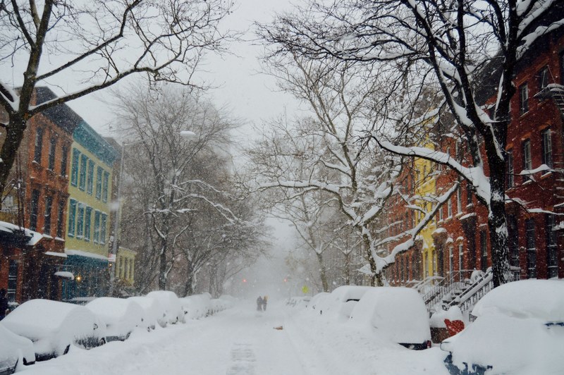 snow covered street cars and trees with two rows of colorful houses, snow covered road 4k