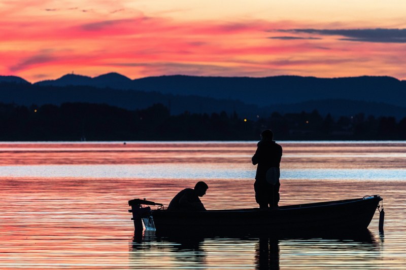 silhouette of two men on a boat gliding across the hallwilersee waters in meisterschwanden during sunset, sunset fishing 4k