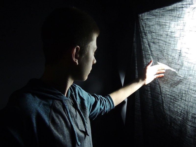 a boy touches the tear of a piece of cloth where light is coming in, _boy touches tear cloth 4k