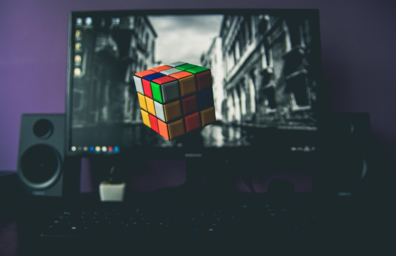 colorful rubiks cube floats in front of computer monitor and speakers, cube 4k