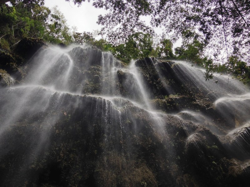 a light waterfall cascading down the side of a rocky cliff lined with trees, wide waterfall 4k