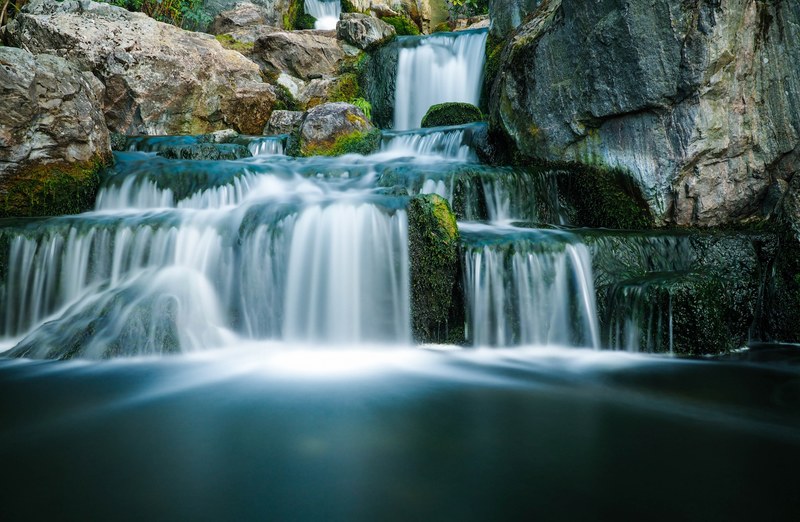a staggered waterfall in motion flowing through a mossy rock mountain in holland park, the japanese garden 4k