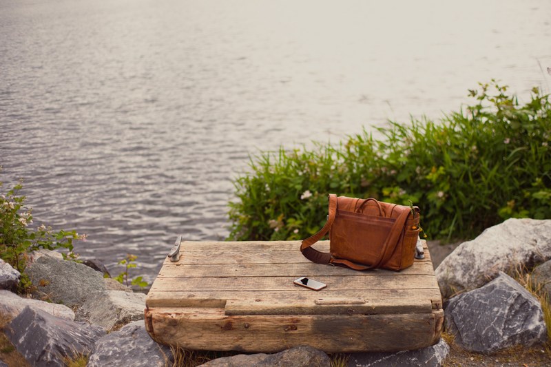 an iphone cellphone and messenger bag on a wooden platform overlooking the water in gas works parks, irene 4k