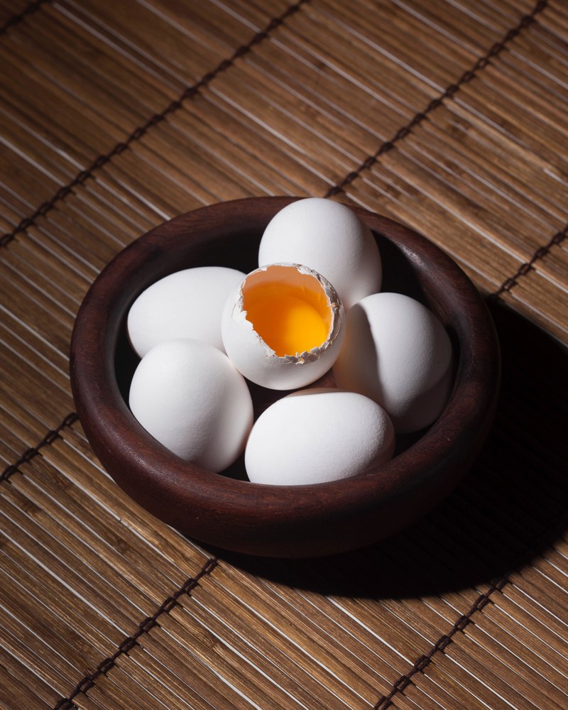 one egg cracks to show the yolk in a bowl full of eggs, bowl of eggs 4k
