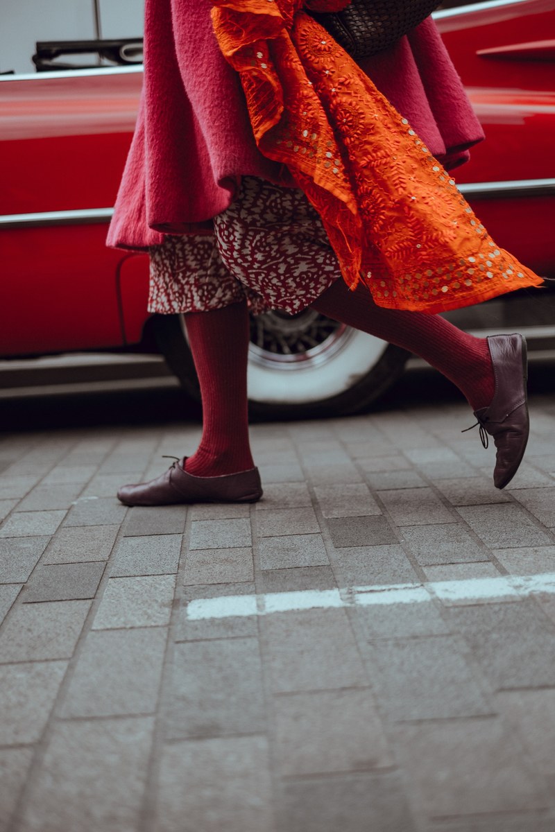 woman dressed in red walking in front of vintage red car at lewis cubitt square, colourful strides 4k