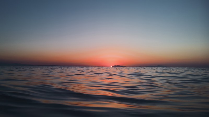 a water level shot looking toward a horizon of low lying lands in messina italy during dawn or dusk sunset turning the sky pink though fades to blue, water level shot looking at the horizon 4k