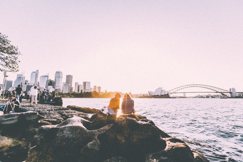 people hanging out by the rocky shores overlooking the sydney harbor on a clear day, clear skies by sydney harbor 4k