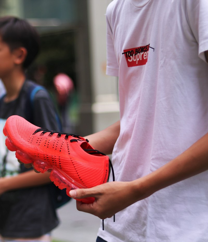 a person wearing a t shirt that says supreme holds a red sneaker with black laces, supreme x clot vapormax 4k