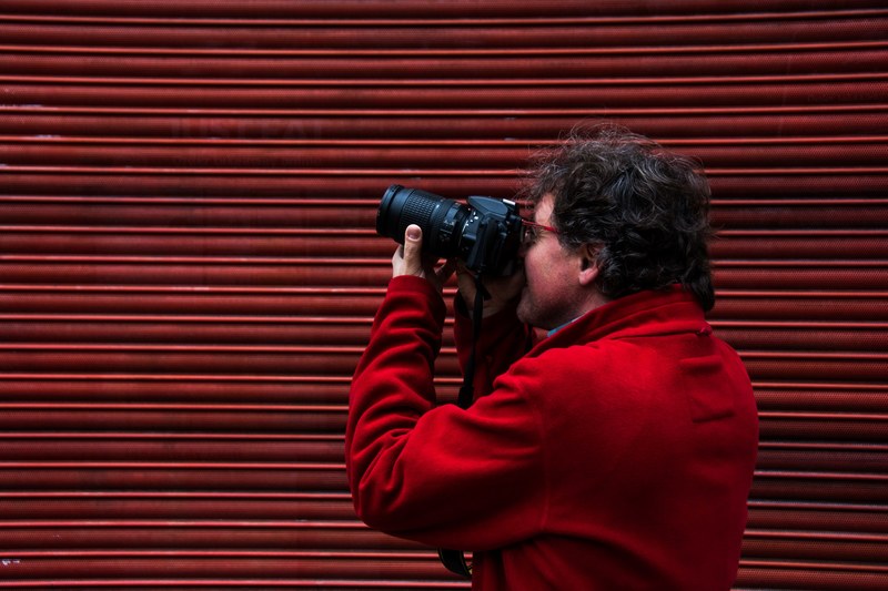 a person in a red jacket points a camera in front of a red wall, red on red 4k