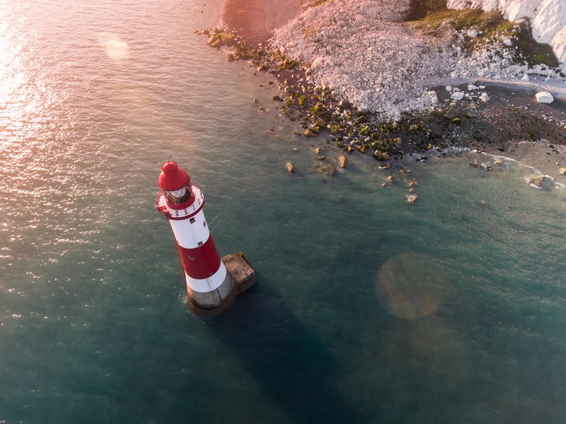 drone view of the red and white lighthouse by the rocky shoreline at eastbourne, lighthouse drone view 4k