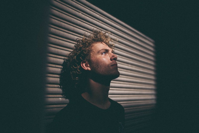 a man with curly hair in shadow leans his head back against a wall, man leaning head on wall 4k