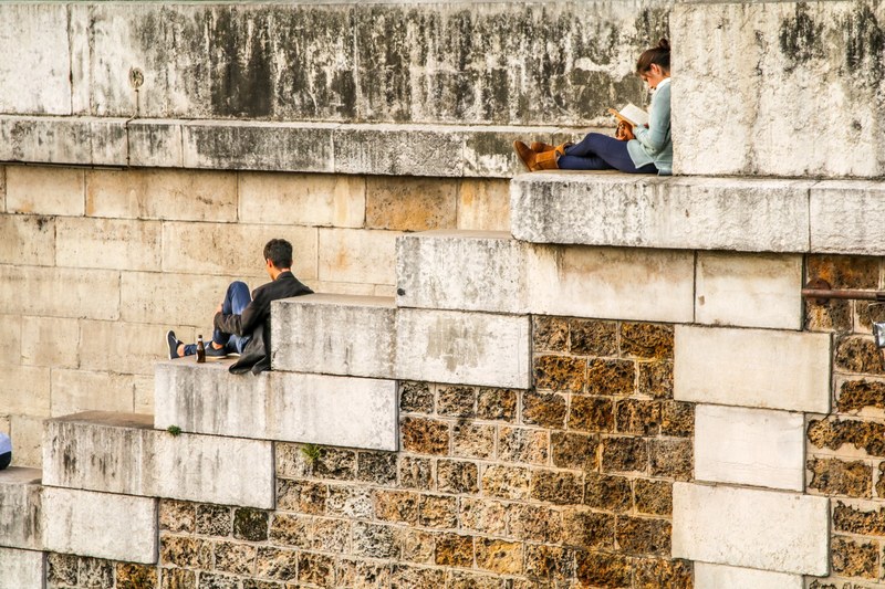 a woman reading a book on brick an stone stairs while a man drinks a beverage, _people sitting on large brick stairs 4k
