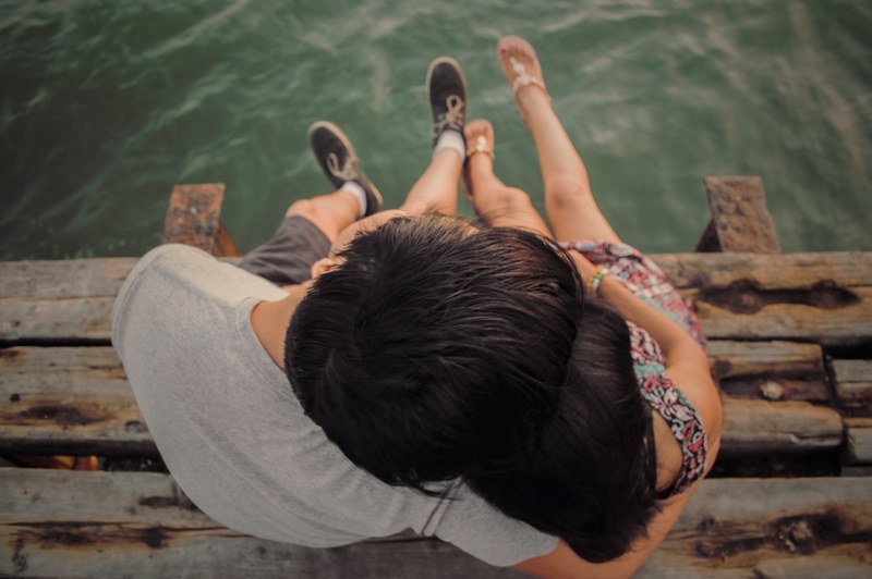 young woman and her boyfriend pictured sitting on a dock with their legs dangling, love 4k