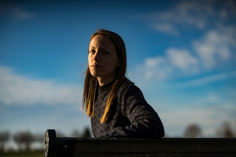 woman sits alone on a park bench in partial shadow, frowing in shadow 4k