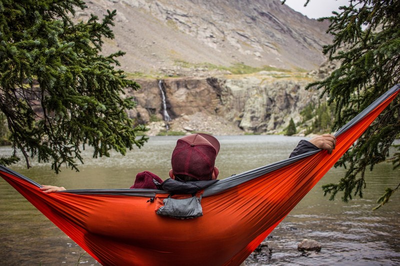 a man relaxes on a red hammock in the mountains by a lake, mountain hammock 4k