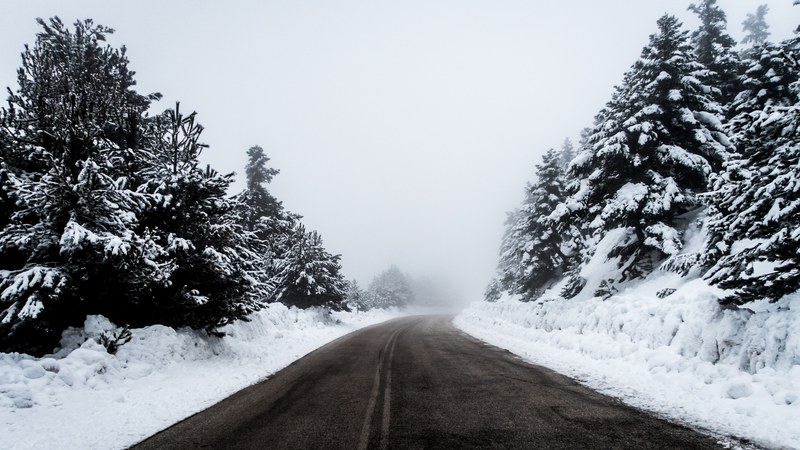 looking down a clean road in ziria greece with snow covered banks and trees on the sides, road by snow covered forest 4k