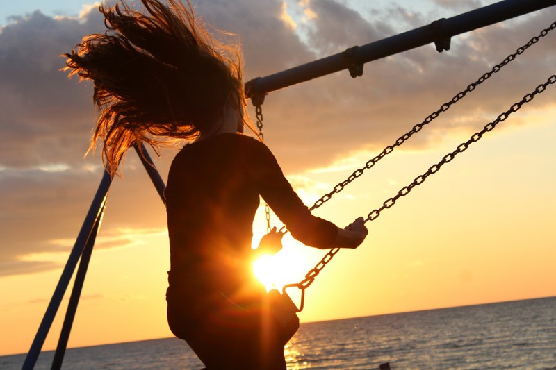 a woman with long hair swings high on a swing near the ocean at sunset, _golden hour swing 4k