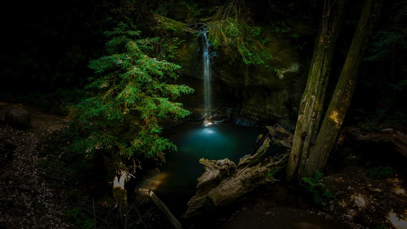 a high angle shot of a waterfall pouring down a rocky ledge into a clear pond in the woods, crystal clear waterfall 4k