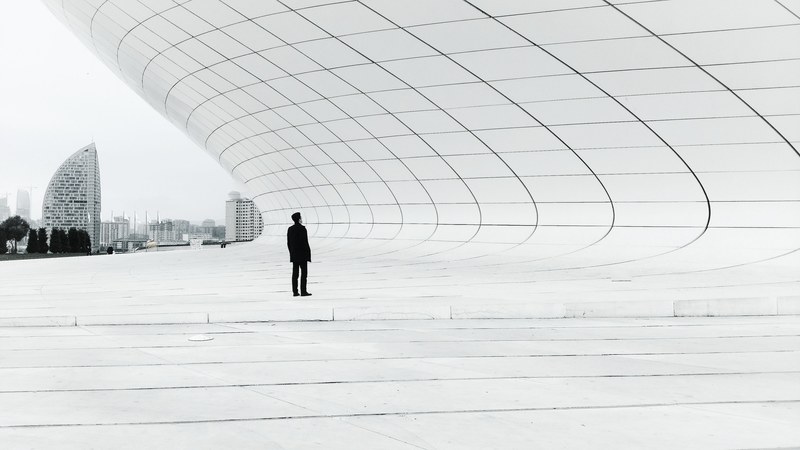 a man dressed in black standing under a wave like white concrete structure, mrblack and mrs_white 4k