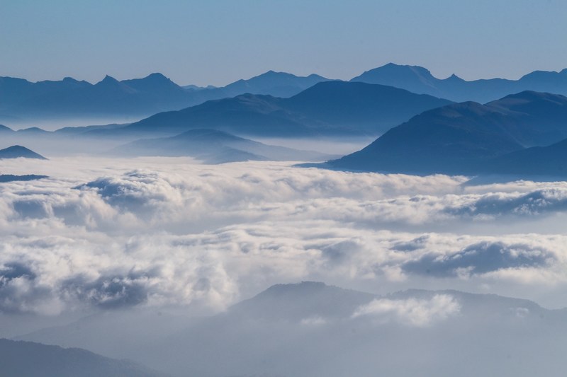 silhouettes of mountains rising up above a thick cover of clouds, mountains emerging from clouds 4k