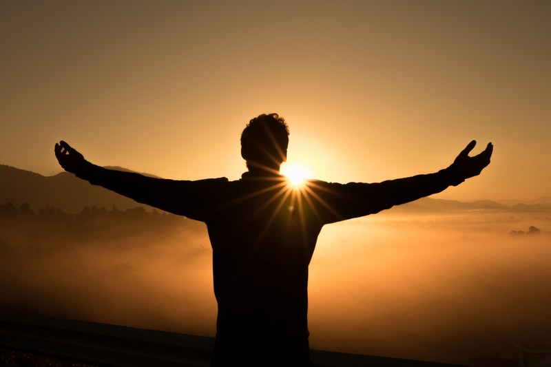 a silhouette man outstretches his arms looking over a valley of fog in chaing mai as the sunrise or sunset turns the sky orange, sunshine bath 4k