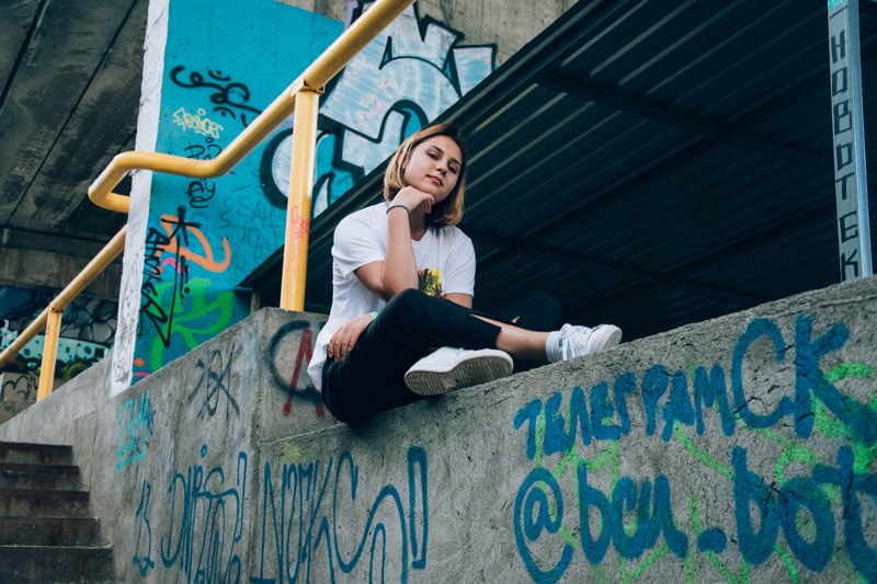 woman in a white t shirt poses on a graffitied concrete wall by stairs and a yellow railing, woman on graffitied wall 4k