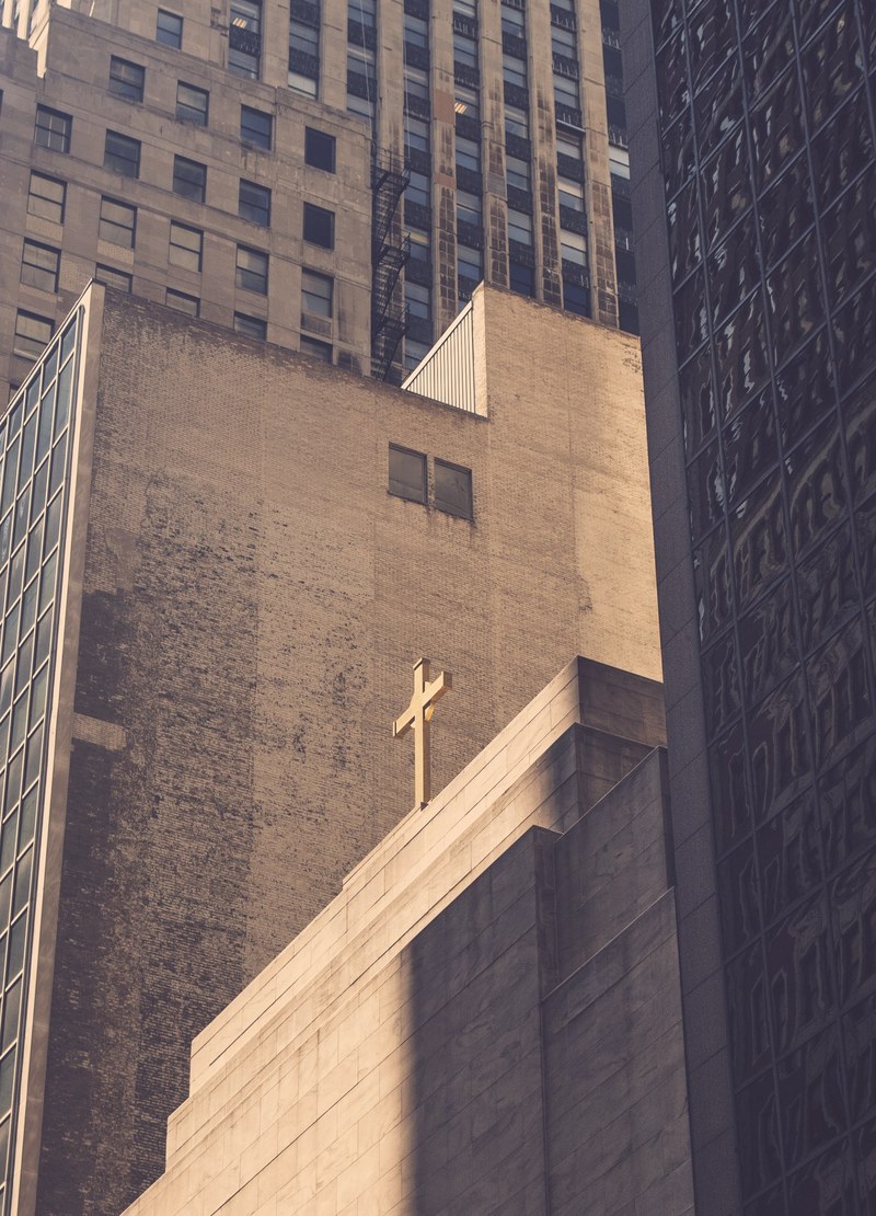 cross on a simple concrete church building surrounded by high rise buildings, cross among skyscrapers 4k