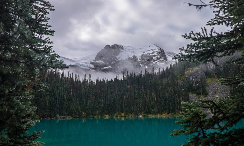 a hidden lake with forests surrounding it and snow covered mountain in the background with a cloudy sky in joffre lakes trail, _hiking joffre lakes in british columbia 4k