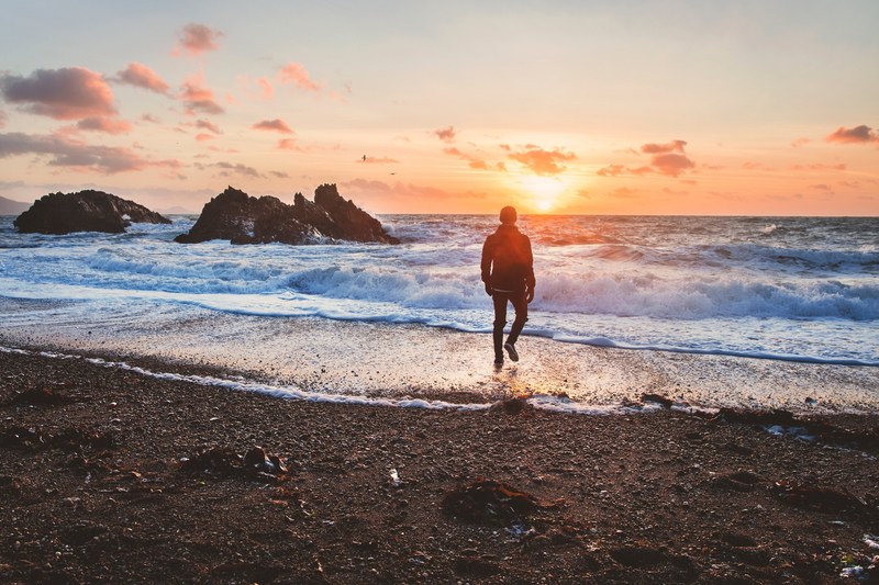 man walking from beach shoreline to the ocean in wales during sunset, exploring wales 4k