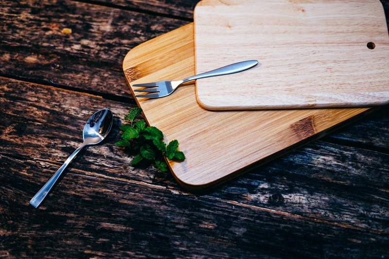two wooden chopping boards on top of each other beside leaves of mint and a metal spoon and fork, cutting boards and cutlery 4k
