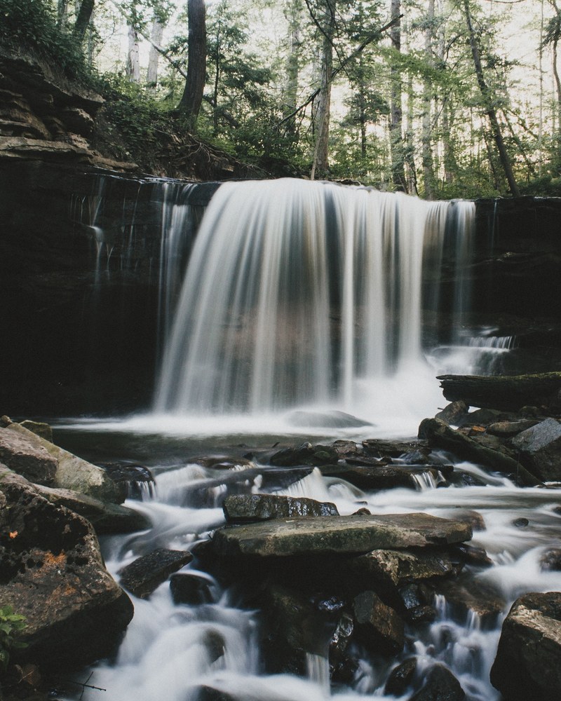 a small waterfall in a forest pouring down on smooth rocks, rocks near a small waterfall 4k