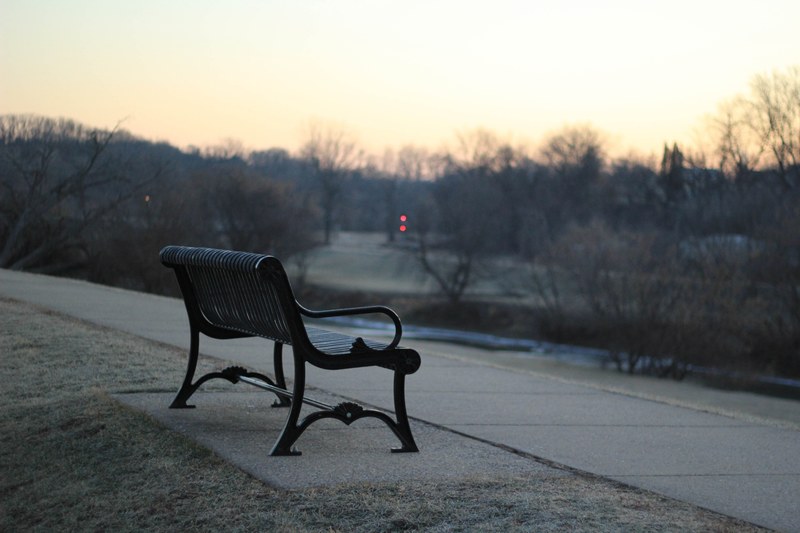 a black bench along an empty park lane during sunset, empty park bench at dusk 4k