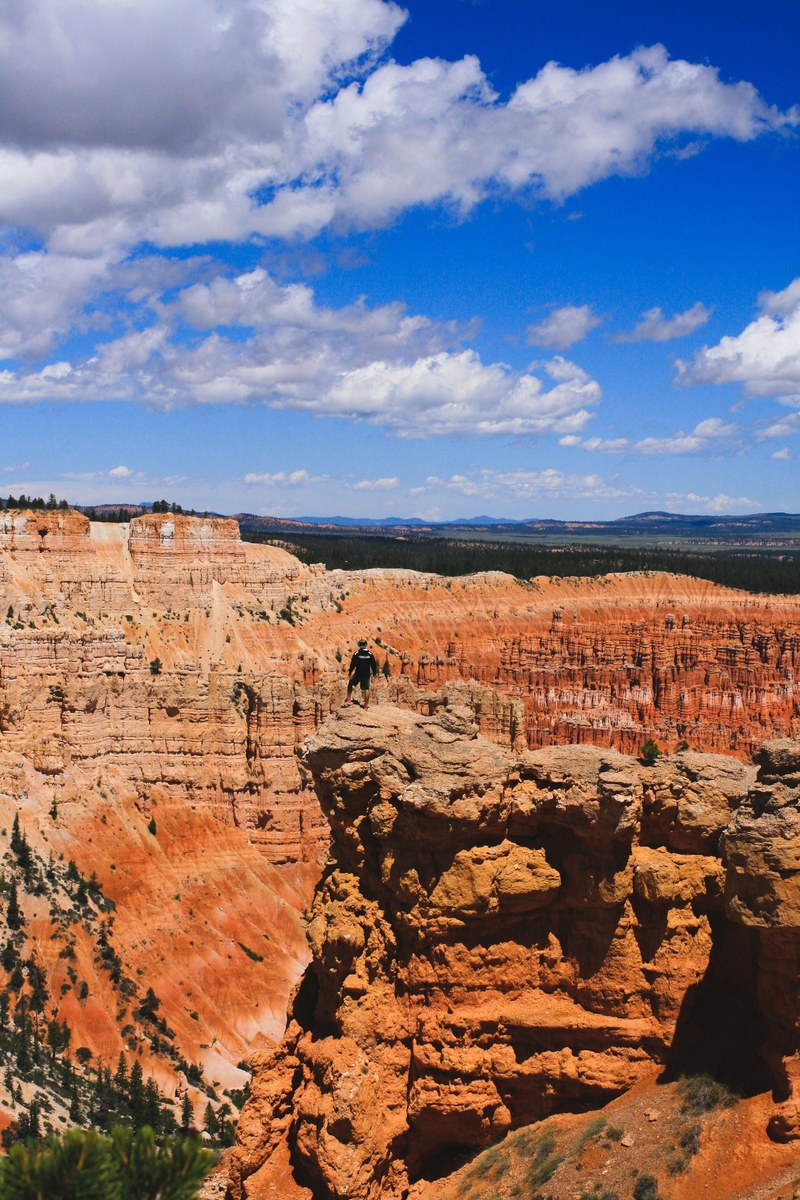 a distant shot of a man standing on a red rock ledge overlooking a deep canyon, looking down into the canyon 4k