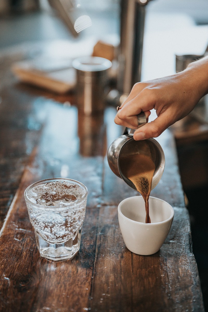 a person pouring coffee into a cup next to a glass of sparkling water, coffee and water 4k