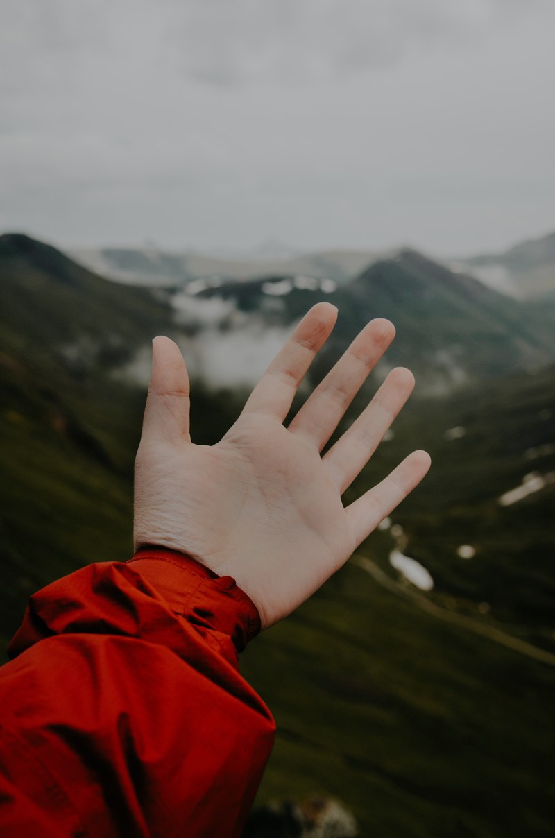 outstretched open hand in front of a foggy mountainscape, reaching for the unknown 4k