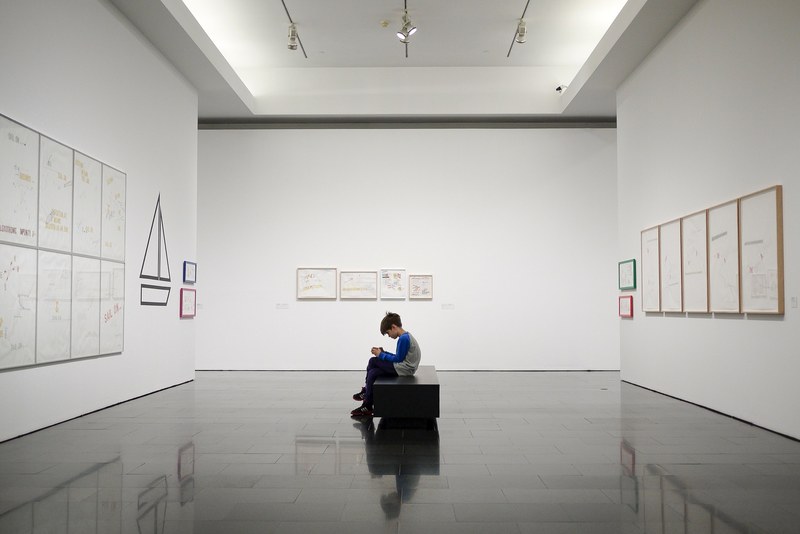 boy sitting alone inside large gallery room with white walls viewing exhibition in barcelona, lone boy barcelona gallery 4k