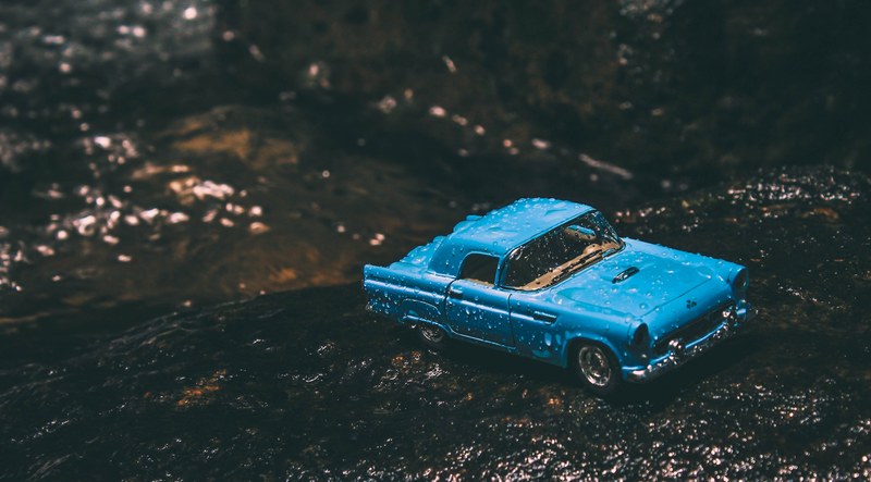 a blue toy car driving through the wet dirt on a forest ground, vintage car toy 4k
