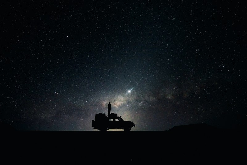 silhouette standing on a jeep roof looking at the starry night sky with nebulas in sossusvlei, observing space 4k