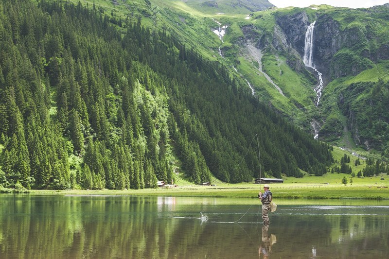 a man fishing while standing in shallow water in a mountain lake, fisherman in a mountain lake 4k