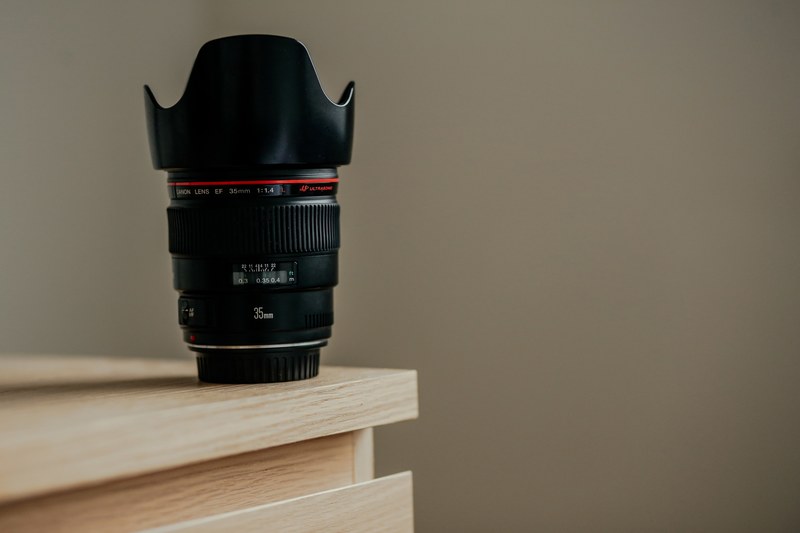 a long camera lens on the edge of a wooden surface, lens and hood on desk corner 4k