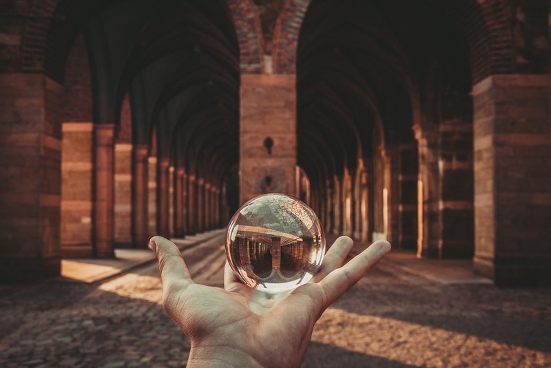 hand holding a reflective glass orb near an arched hallway, orb reflections 4k