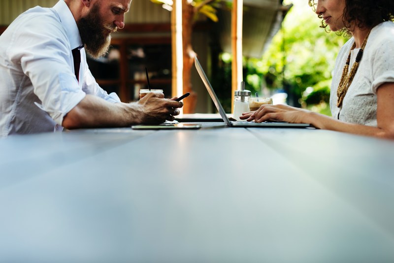 two people sit at a table and one is on a cellphone the other a laptop, people on phone and laptop 4k