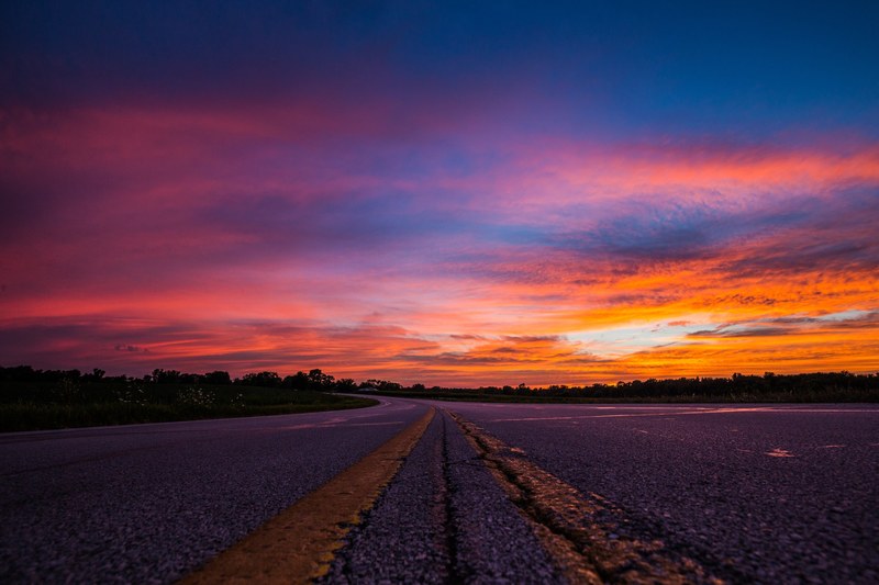a pink orange and blue sunset glow upon the asphalt of a highway road, cool sunset hues on a highway 4k
