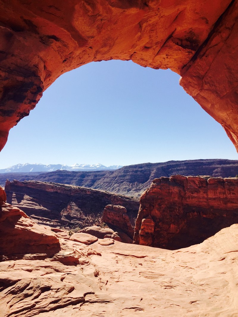 a view on a sunlit canyon from below a red rocky arch, red canyon arch 4k