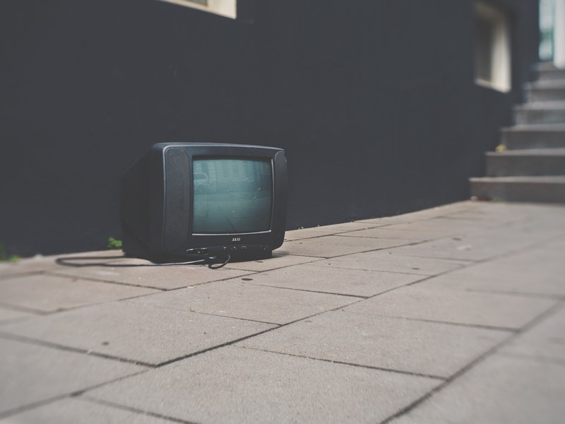 television with cord sitting on sidewalk outside of black building near stairs, television on sidewalk 4k