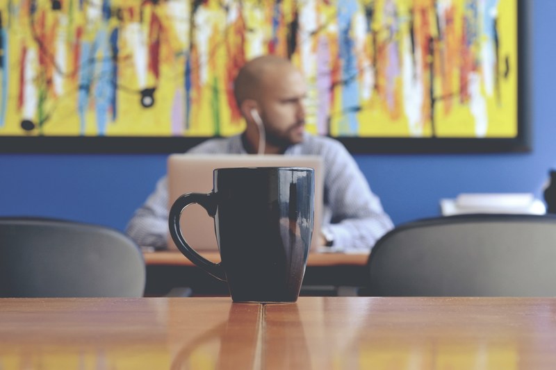 a fuzzy shot of a mug on a table and a man sitting at a laptop at the back of the room, working man behind a mug 4k