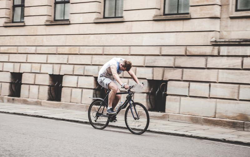 a man rides a bicycle next to the curb on a street in cambridge looking down, man riding bicycle 4k