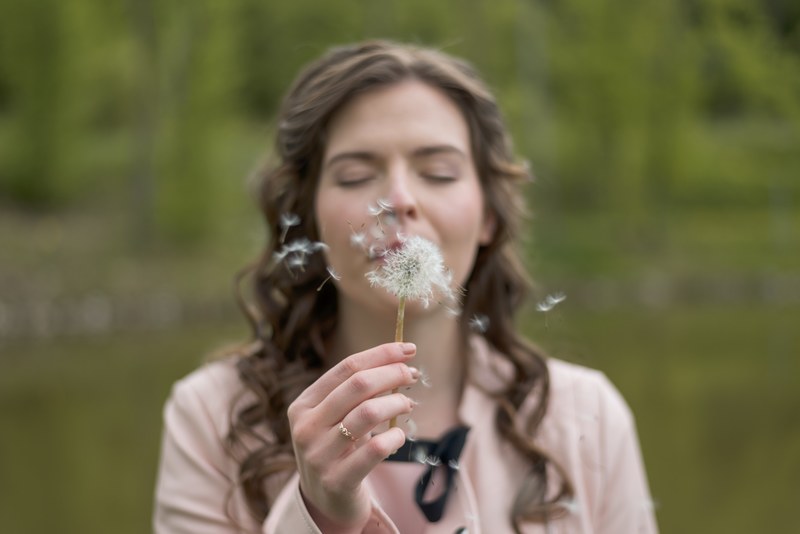 a woman with eyes closed blows seeds from a dandelion against a green background, woman blowing dandelion 4k