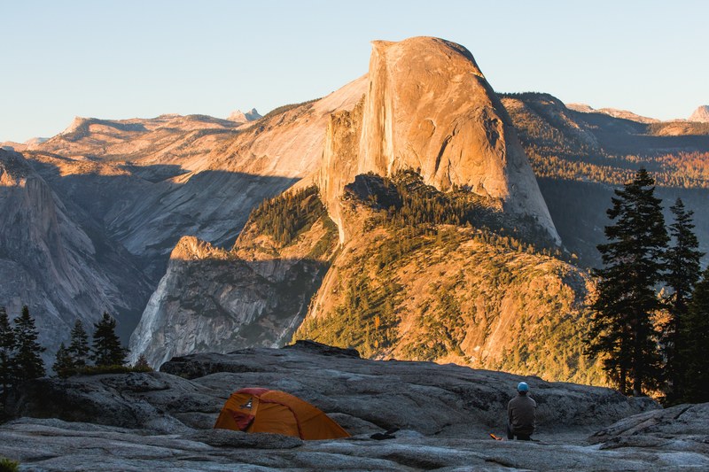 a hiker crouching near a tent during golden hours in yosemite valley, some places make you feel really small 4k